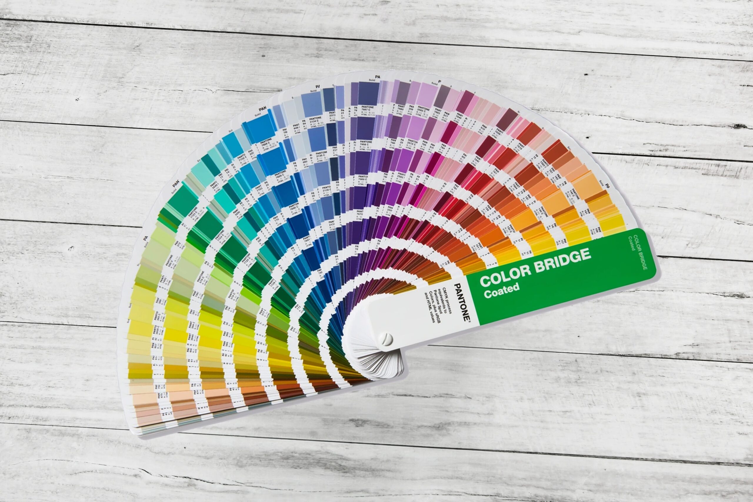 Guía Pantone Color Bridge Coated desplegada en abanico sobre fondo de madera clara, mostrando una amplia gama de colores.