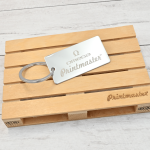 Llavero tipo tag rectangular en acero inoxidable grabado con láser, con logo de Omega Printmaster sobre base de madera.
