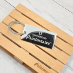 Llavero tipo tag rectangular en acero inoxidable grabado con láser, con logo de Omega Printmaster sobre base de madera.