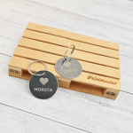 Dos tags circulares de acero inoxidable grabados con láser con los nombres “Morita” y “Angie”, apoyados sobre mini pallet de madera grabado con el logo Printmaster.