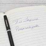 Lapicera Prestige Negra personalizada de Imprenta Omega sobre cuaderno con la frase “Tu lapicera personalizada” escrita a mano.