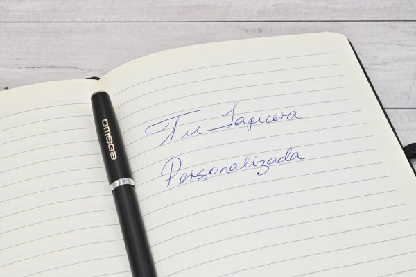 Lapicera Prestige Negra personalizada de Imprenta Omega sobre cuaderno con la frase “Tu lapicera personalizada” escrita a mano.