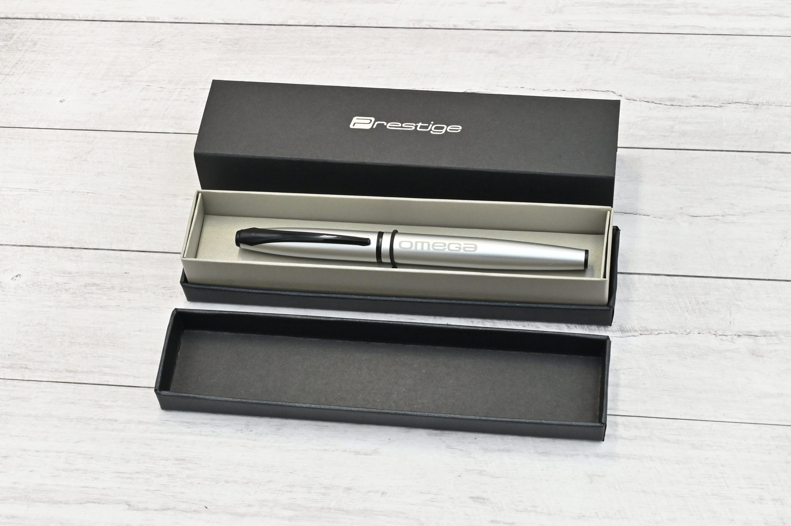 Lapicera Prestige Silver personalizada de Imprenta Omega sobre cuaderno abierto, con cuerpo metálico plateado y tapa negra.