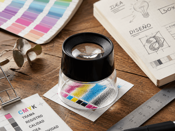 Cuenta hilos profesional 10X inspeccionando una trama CMYK sobre una mesa de trabajo de diseño gráfico e impresión.