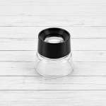 Cuenta hilos profesional 10X de enfoque fijo con lente óptica y base transparente sobre fondo de tablones blancos.