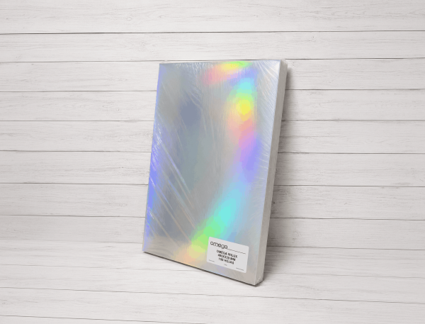 Paquete de papel metalizado iridiscente Omega Irilux de 485x330 mm y 100 hojas, presentado sobre fondo blanco estilo estudio con reflejos holográficos multicolor.