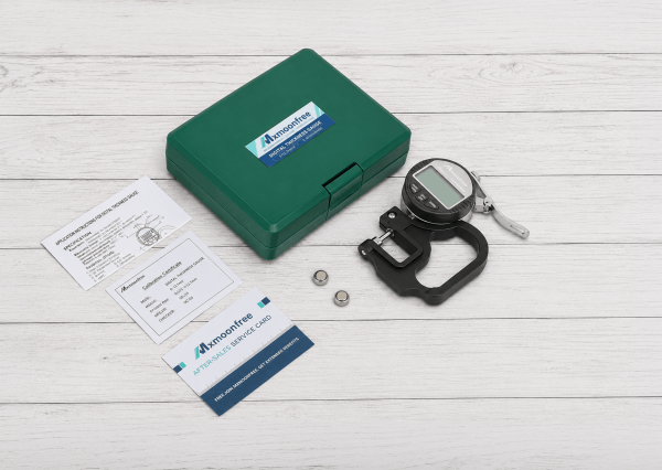 Kit completo del medidor digital de espesor con estuche rígido, baterías LR44, certificado de calibración y documentación sobre fondo de madera blanca.