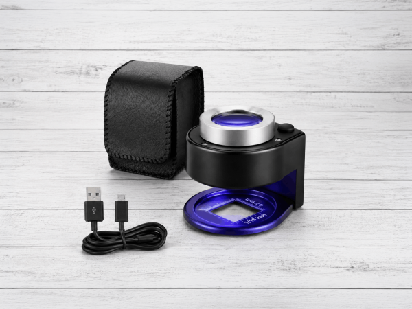 Cuenta hilos profesional 30X recargable con iluminación LED blanca y UV, estuche protector y cable USB sobre fondo gris neutro.