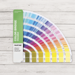Guía Pantone Color Bridge Uncoated abierta en abanico sobre superficie de madera blanca, mostrando referencias Pantone y equivalencias CMYK para impresión profesional.