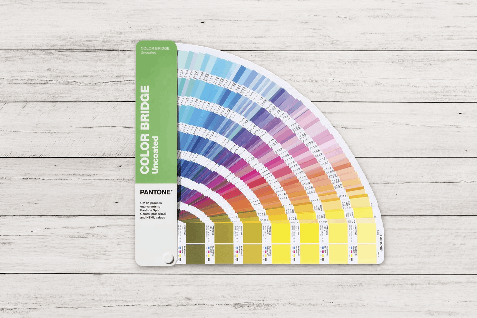 Guía Pantone Color Bridge Uncoated abierta en abanico sobre superficie de madera blanca, mostrando referencias Pantone y equivalencias CMYK para impresión profesional.
