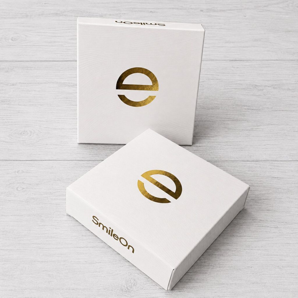 Cajas rígidas personalizadas SmileOn en cartulina blanca con textura y stamping dorado, presentadas en diferentes posiciones sobre fondo de madera clara.